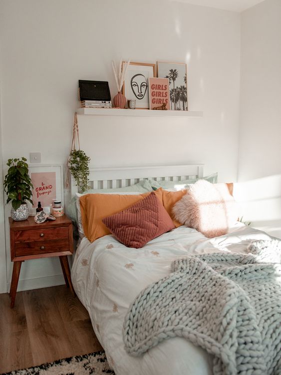 A cool, modern teen room with a bed and colorful linens, a stained nightstand, a gallery wall and plants