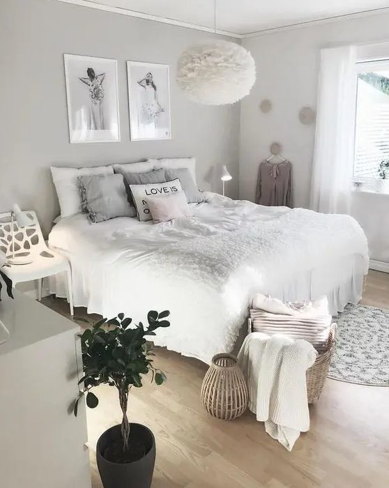 A cool, neutral teenage girl's bedroom with a gray accent wall, a bed with neutral linens, a white chair, a dresser, some artwork and a fluffy lamp