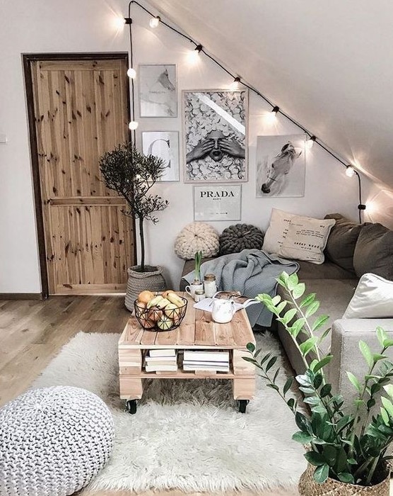 A cozy boho living room in the attic with a credenza, pallet table, layered rugs, gallery wall, fairy lights and a crochet stool
