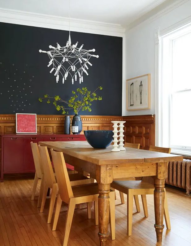 a cozy dining room with a soot-colored accent wall, stained panels, a red sideboard, a vintage dining table and chairs, and a creative chandelier