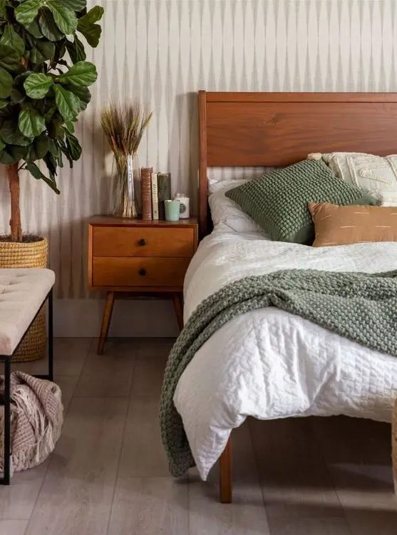 a cozy earth-tone bedroom with a stained bed and neutral linens, a stained bedside table, an upholstered bench and a potted plant