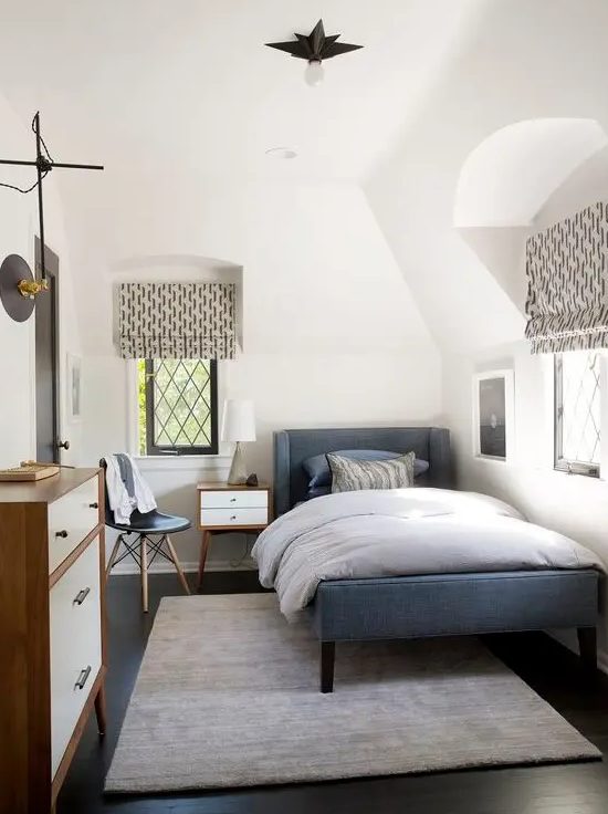 A cozy mid-century modern teen bedroom with a blue upholstered bed, dresser, printed textiles, small nightstand and chair