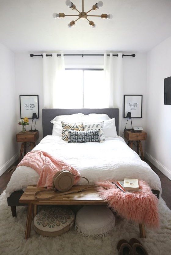 a cozy little bedroom with stained bedside tables, a bed with neutral linens, a bench, some pink blankets and pillows