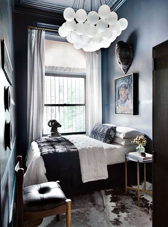 a dramatic and small bedroom with dark walls and ceiling, dark and chic furniture, a cluster chandelier and a gallery wall
