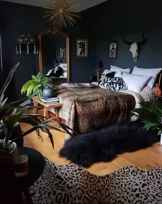 a glamorous, atmospheric bedroom with wooden furniture, an oversized gold-framed mirror, a sunbeam chandelier and faux animal skis