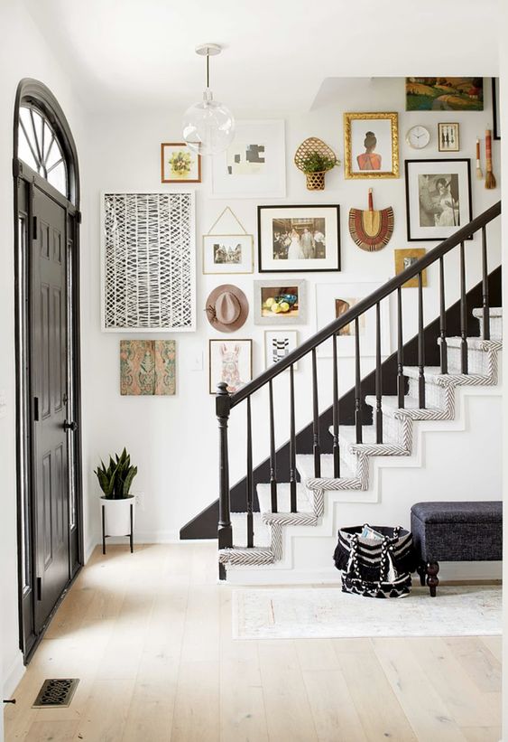 A beautiful entryway with a colorful gallery wall above the stairs, not only with artwork and photos, but also hats, greenery and fans