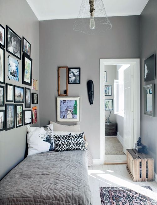 a gray, narrow bedroom with a small bed, a storage box and gallery walls and a pendant lamp