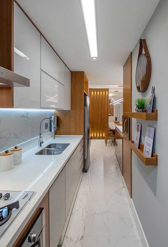 a long, narrow kitchen with sleek white and gray cabinets, moldings, built-in lights and pretty decor