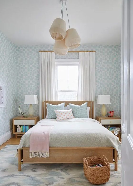 A beautiful and calm teenager's room with blue wallpaper, a stained bed with pastel linens, stained bedside tables and hanging lamps