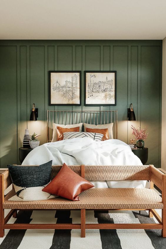 A pretty boho bedroom with a modern, earthy feel, green paneling, a bed with neutral linens, a bench with pillows and sconces