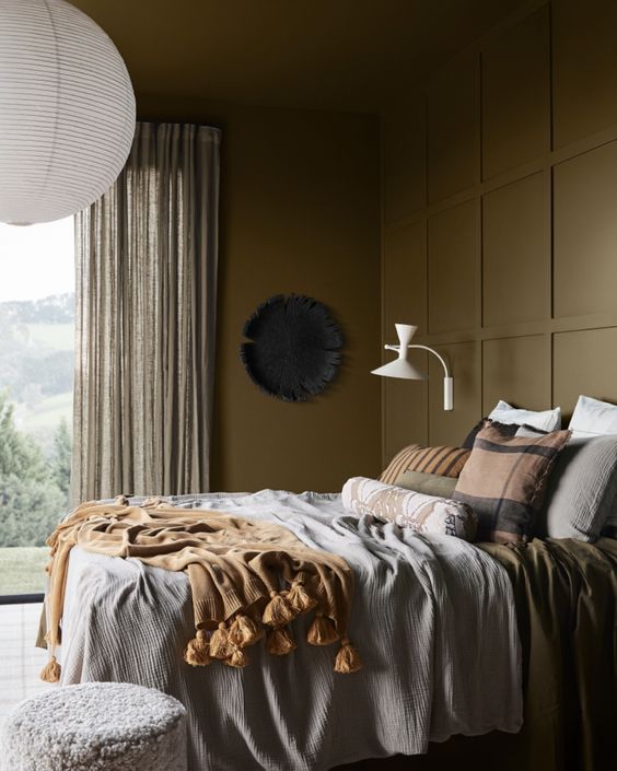 A beautiful earth toned bedroom with brown walls, a bed with earthy linens, some lamps and a cool outdoor view