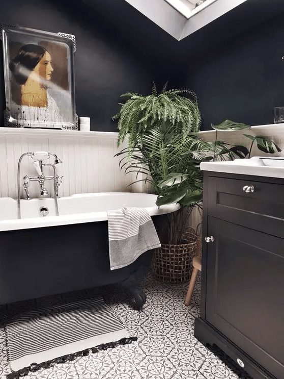 a beautiful modern bathroom with black walls, white floorboards, a black vanity, a black bathtub, patterned tiles, a skylight and a piece of art
