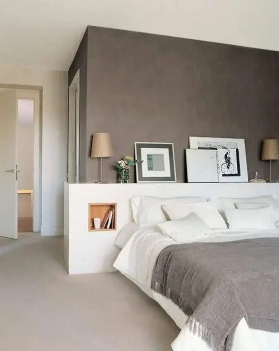 A beautiful, modern bedroom with a taupe accent wall, white bed with storage headboard, artwork and lamps, and white linens