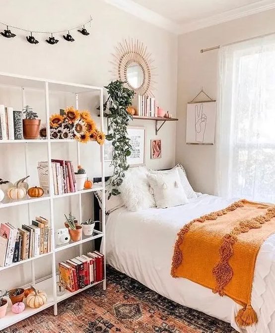 A pretty teenager's room with a black bed, a large open shelf with flowers and pumpkins, a shelf and a mirror above the bed