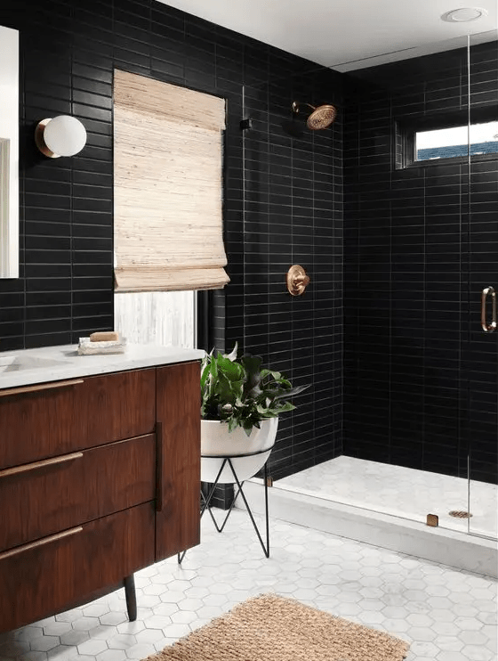 a mid-century modern bathroom with thin black and white hex tiles, a stained vanity, shower area, brass fixtures and potted plants