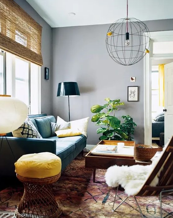 A mid-century modern living room with gray walls, a green sofa, some stained furniture, a statement stool, a spherical pendant lamp and a potted plant