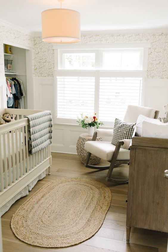 A small, mid-century modern nursery with an open closet, a neutral crib, a white chair, a stained dresser and some printed textiles