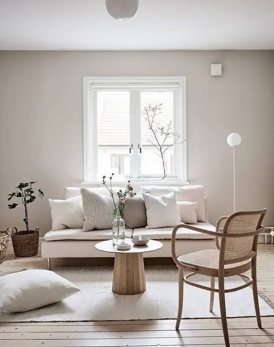 a minimalist, neutral living room with a pink love seat, a rattan chair, neutral pillows and some greenery