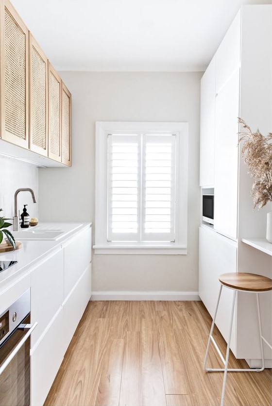 a minimalist white galley kitchen with elegant cabinets, rattan upper cabinets, a wooden stool and some grass