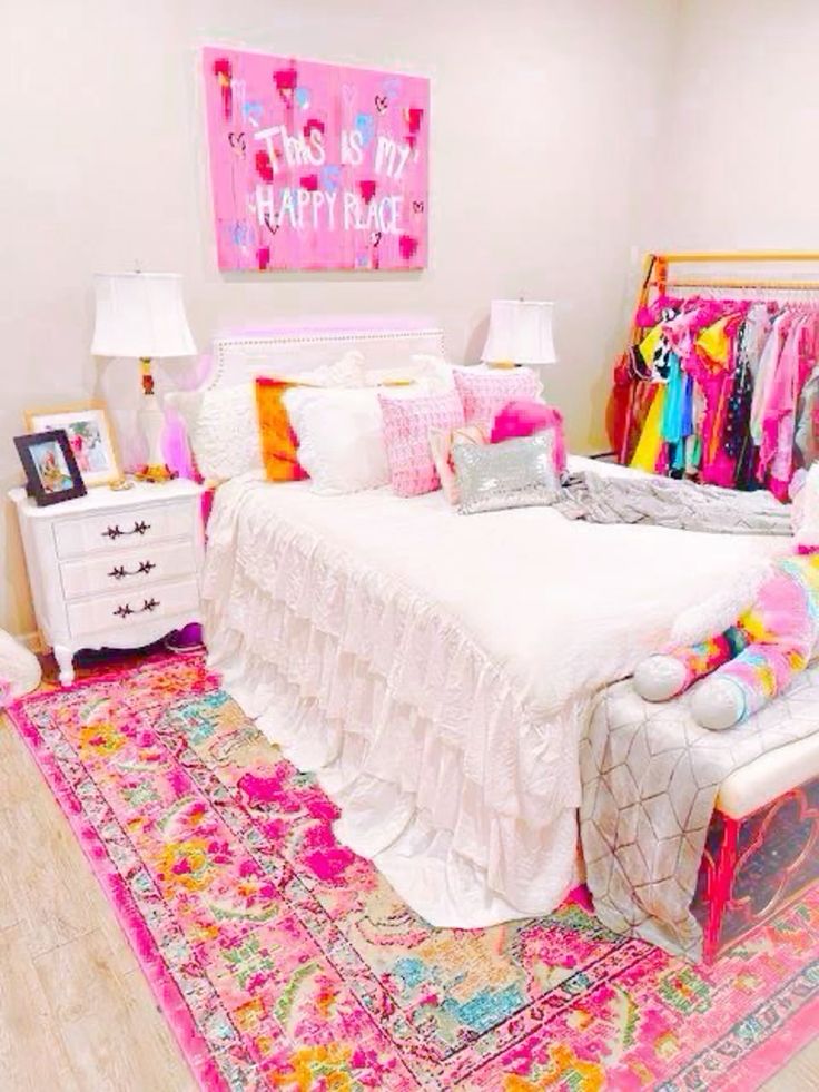 A modern and bright teenage girl's room with a bed with pink linens and a bold pink carpet, a makeshift wardrobe, bedside tables with lamps and a bench
