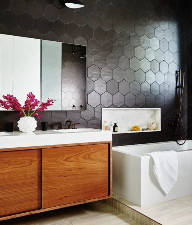 a modern bathroom with soot-colored hexagon tiles, neutral tiles, a richly stained vanity, a bathtub and a mirrored cabinet
