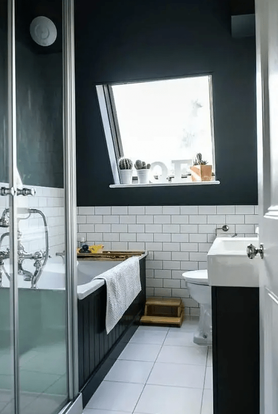 A modern black and white attic bathroom with a black boarded bathtub, a black vanity with a white sink and a square tiled floor