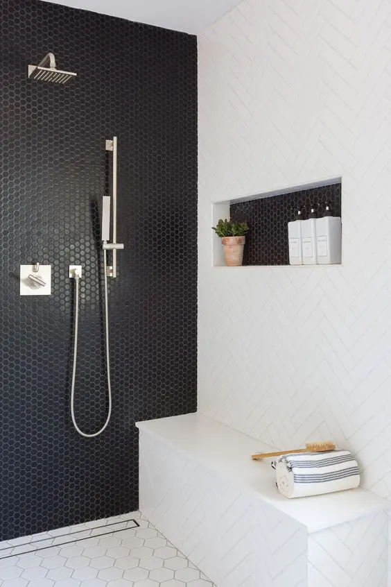 a modern black and white shower area with a penny tile wall and a herringbone wall, a hexagonal tile floor and a niche shelf