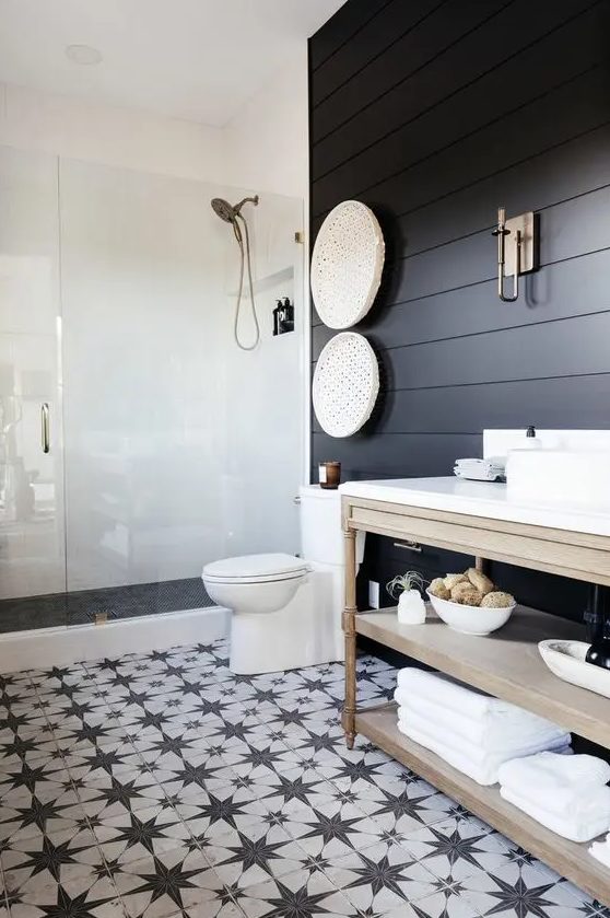 a modern farmhouse bedroom with sooty shiplap walls, a shower area, a light stained vanity and a black and white star tile floor