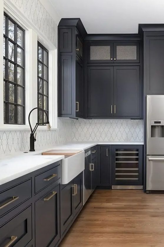 A modern farmhouse kitchen with soot cabinets, a white tile backsplash, white stone countertops and brass handles