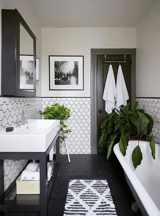a modern monochrome bathroom with printed tiles, a large sink, a vintage bathtub, a mirrored cabinet and lots of greenery