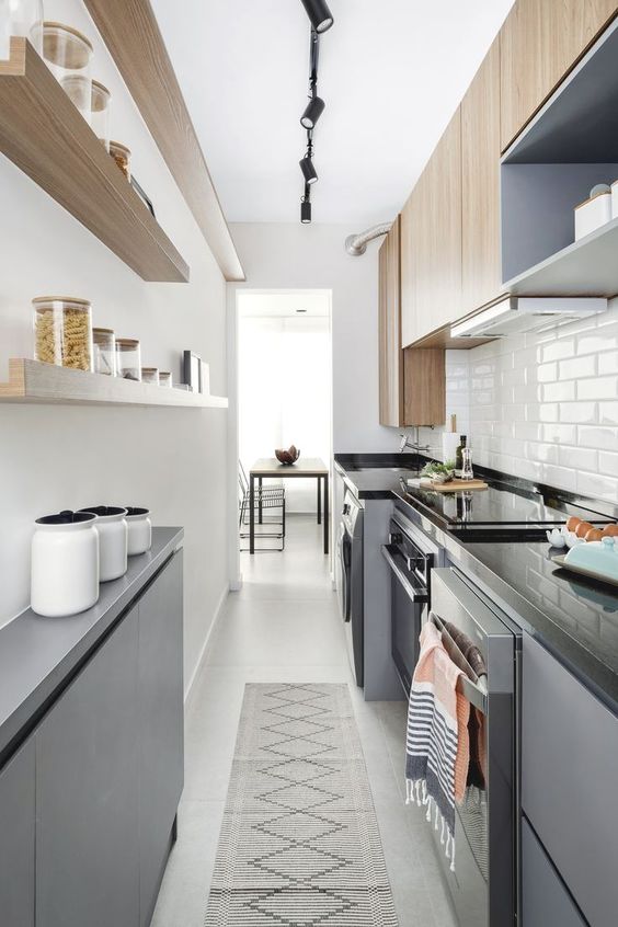 a modern, narrow kitchen with sleek gray cabinets, black stone countertops, open shelving and stained cabinetry, and a printed rug