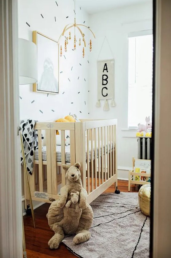 a modern small children's room with a stained cot with printed bedding, a changing table, a shelf and some mobiles and toys