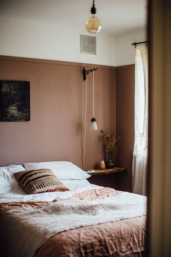 A moody and earthy guest room with a bed and earthy linens, a living edge nightstand and a pendant lamp