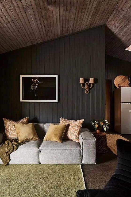 a moody living room with a soot patterned wall, a gray low sofa, a yellow carpet, a piece of art and some bright cushions
