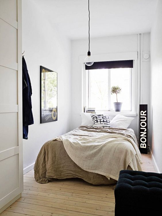 A narrow bedroom in neutral tones and black with a black sign, a pendant lamp and a black stool is a cool idea