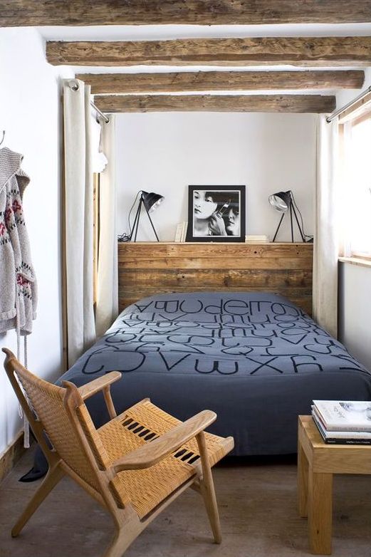 a narrow bedroom with a reclaimed wood headboard as a bedside table, wooden beams, a chair and a table with books