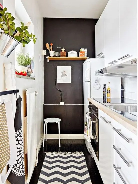 a narrow kitchen with sleek white cabinets, butcher block countertops, a chalkboard wall, printed textiles, and herbs in planters