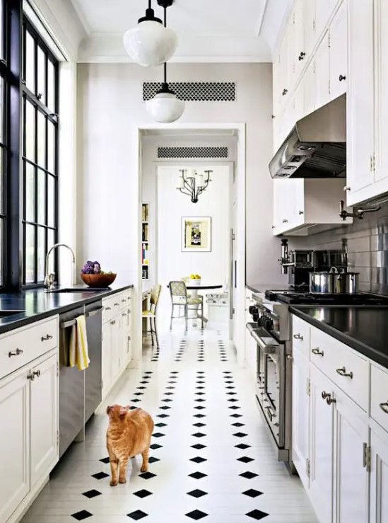 a narrow kitchen with white shaker-style cabinets, black countertops, a checkered floor, and some pendant lamps