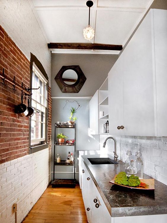 a narrow modern kitchen with brick walls, white cabinets, stone countertops, open shelving and pendant lamps