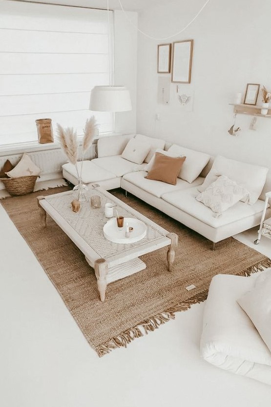 A neutral boho living room with a white sofa, a woven table, a jute rug, pampas grass, a gallery wall and lots of pillows