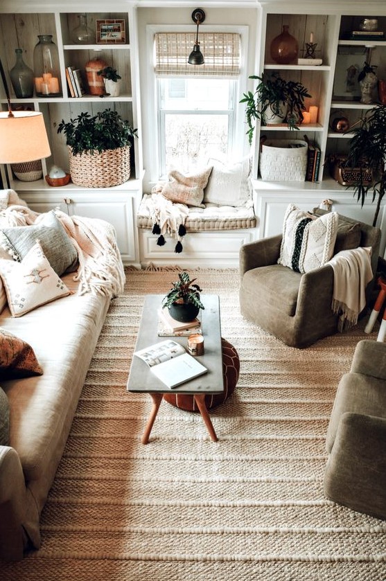 A neutral boho living room with lots of texture, potted plants, a sofa, chairs and a window seat, as well as a leather ottoman