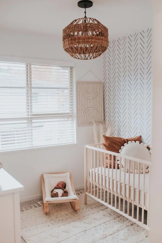 a neutral boho nursery with a white dresser, a stained crib, a small rocker for the baby, an accent wall and a printed rug