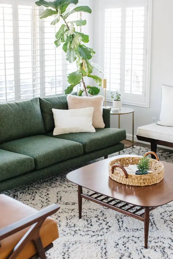 A neutral living room with a green sofa, a light brown and a white chair, a coffee table and some greenery in a pot looks inviting