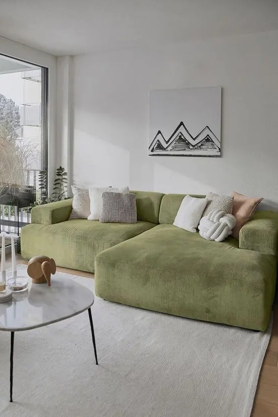 a neutral living room with a low green sofa and neutral pillows, a coffee table with some decor, a neutral rug and a fun piece of art