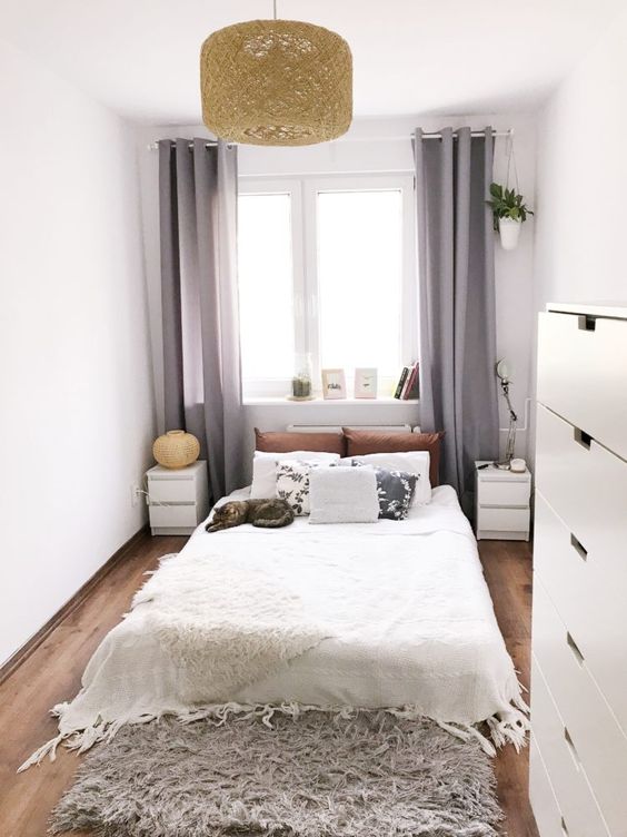 a neutral, narrow bedroom with a bed, matching nightstands, a fluffy rug, a pendant lamp and a dresser