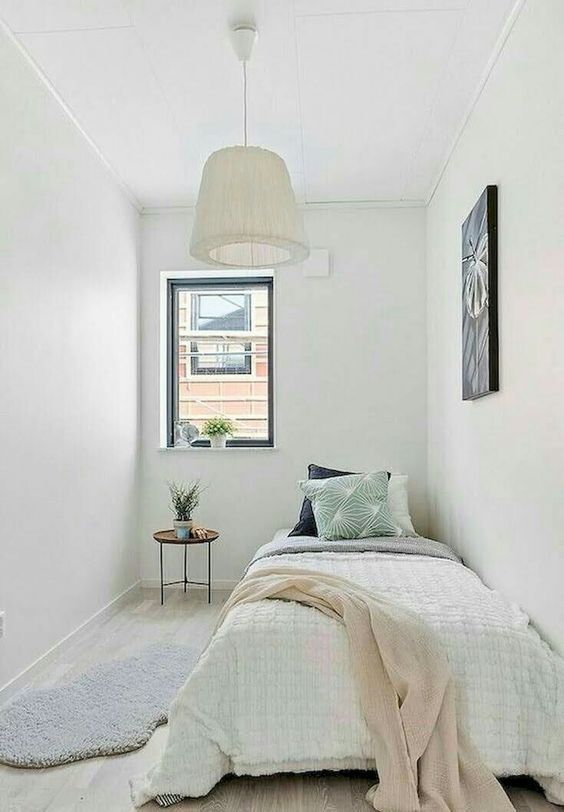 A neutral, narrow bedroom with a bed, some art, potted plants, and a pendant lamp makes a cool guest room