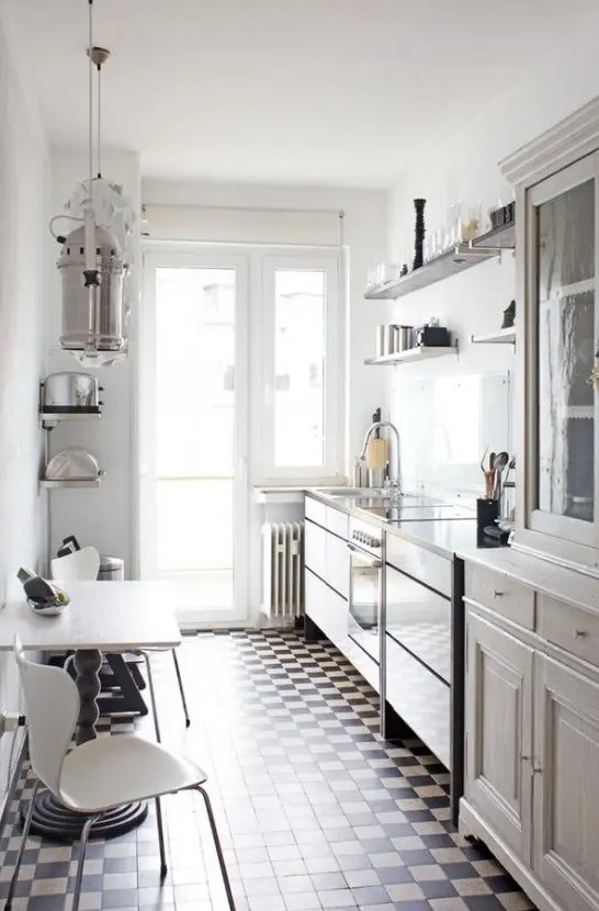 a neutral, narrow kitchen with vintage cabinets and open shelves, a checkered floor, a table and white chairs and pendant lamps