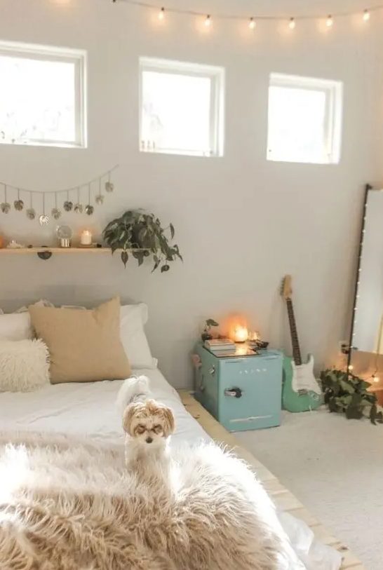 a neutral teen room with neutral walls, a pallet bed, a floor mirror, a blue cabinet, a floating shelf with green plants and candles and a guitar