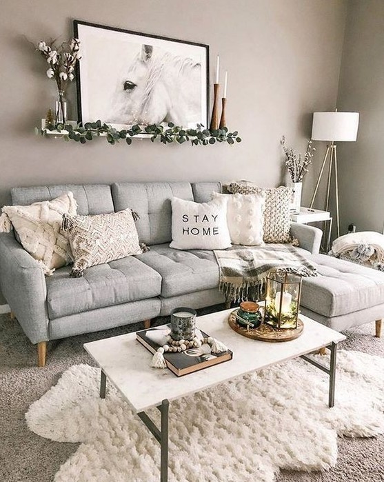 A pretty boho living room with a gray sofa, a white table, layered rugs, neutral tables, some candles and a piece of art
