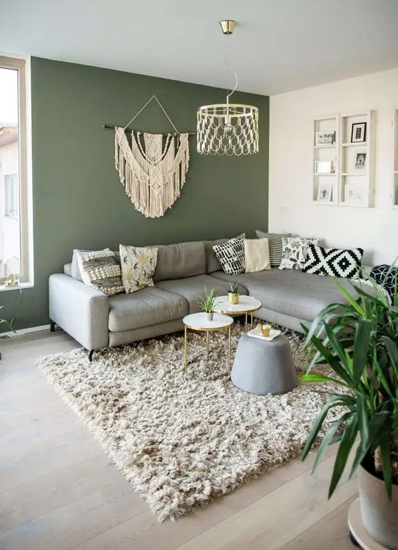 a pretty living room with a green accent wall, a gray cabinet, some boho decor and printed pillows, a fluffy rug and coffee tables